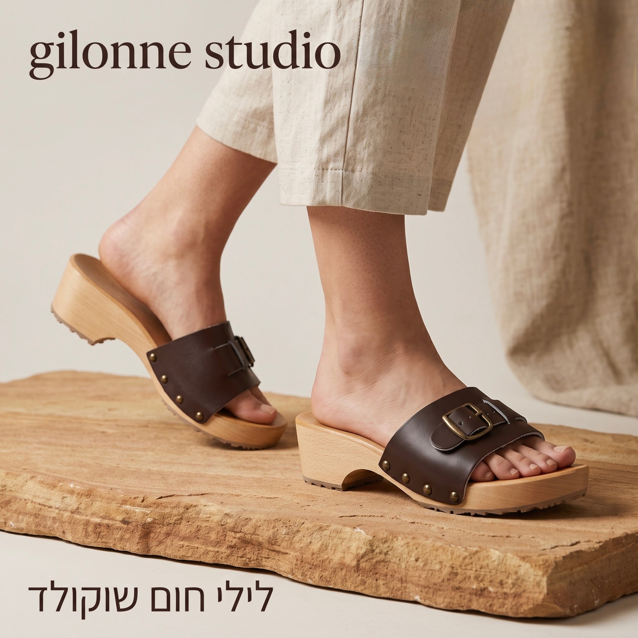 רגליה דוגמנית בצילום תקריב עם מכנסי כותנה בהירה, קבקבי-עץ פתוחים דגם לילי של ג׳ילון-סטודיו, בתמונת צעידה סטטית על מצע אבן הבטתי כמו במה נמוכה וכיתוב ״לילי חום שוקולד״