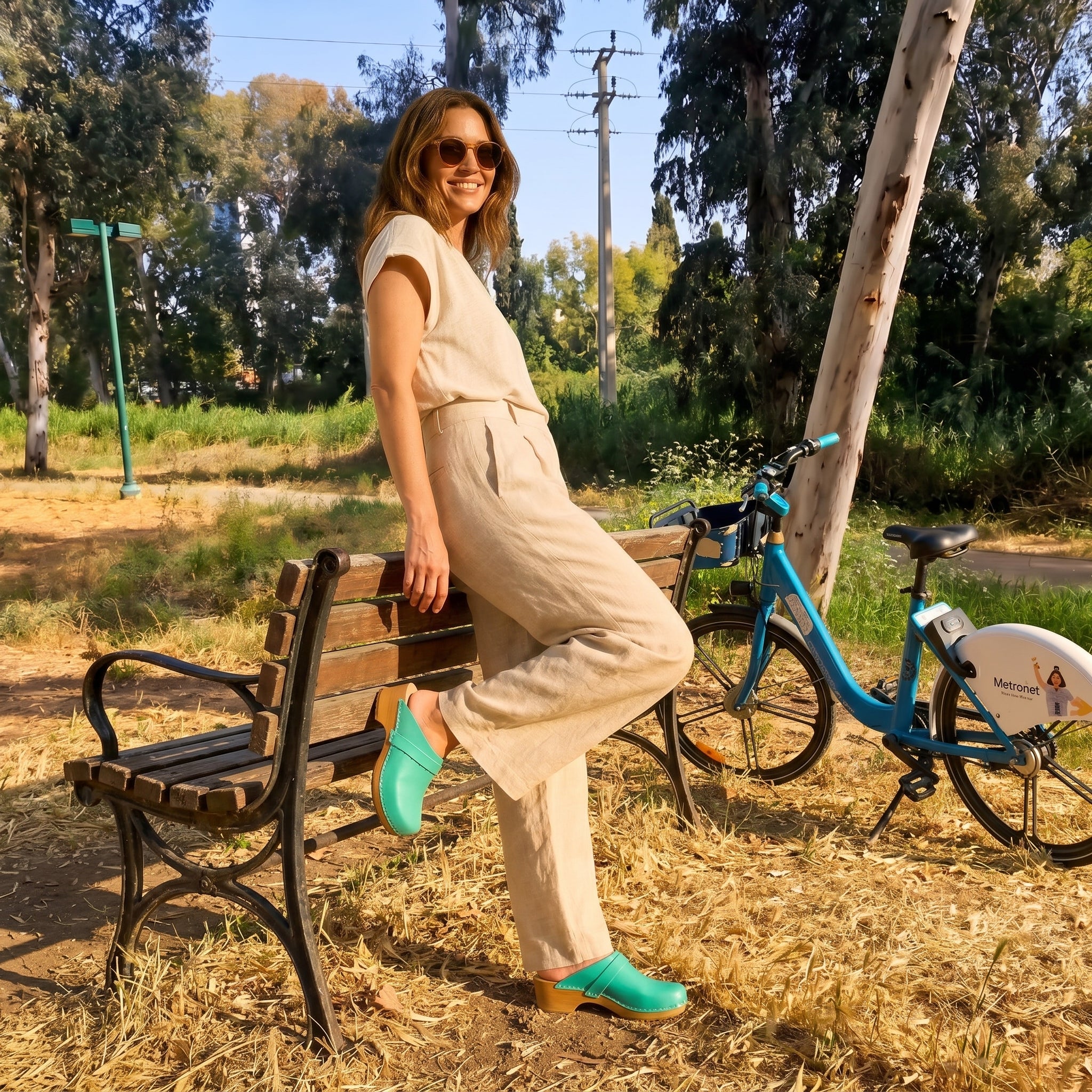 בחורה בפרק הירקון נועלת קבקבי עץ של ג׳ילון בצבע ירוק פיסטוק ליד אופניים