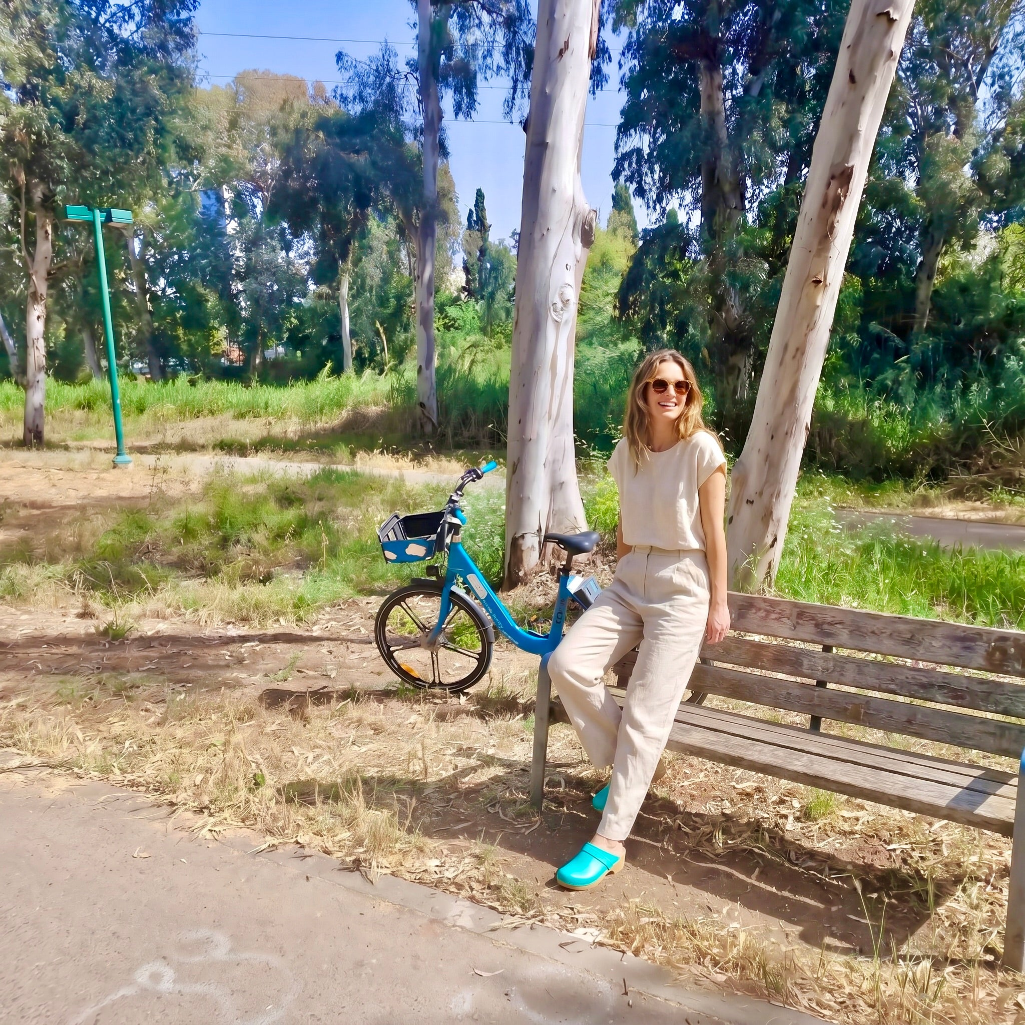 אשה בפארק הירקון רמת גן ליד ספסל נועלת קבקבי עץ בצבי ירוק מעלף פיסטוק ג׳ילון סטודיו מקולקציית קבקבי-העץ השוודיים של ג׳ילון סטודיו